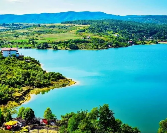 Vibrant blue waters of Cincis Lake with lush hills and scattered houses.