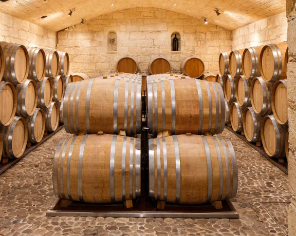 Historic wine cellar with large oak barrels stacked in rows inside stone walls.