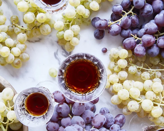 Close-up of white and red grape clusters with glasses of sweet Cypriot wine on a marble table.
