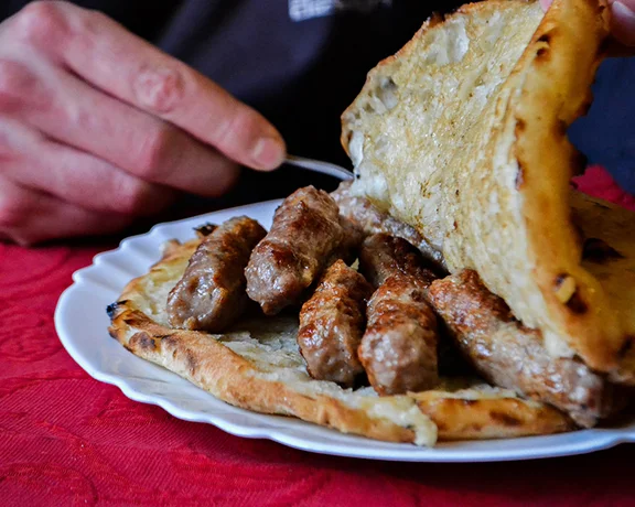 Plate of grilled Serbian ćevapi sausages served inside flatbread.