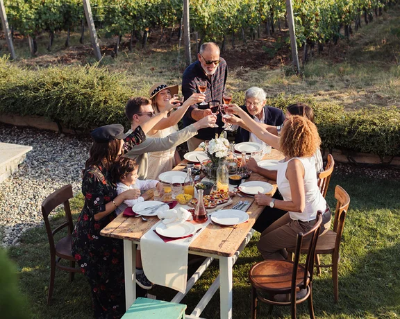 Family gathered outdoors in a vineyard in Serbia, raising glasses for a celebratory meal.