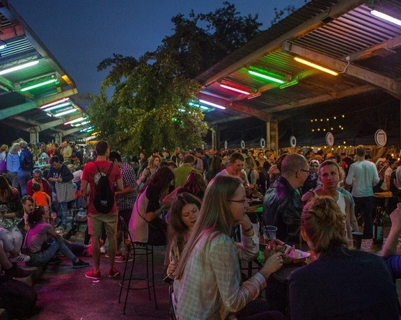 The vibrant energy of a Warsaw night market, alive with colorful lights, bustling crowds, and the fresh air of the open sky.