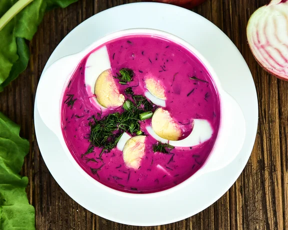 Polish barszcz made of beetroots served with egg and dill on a plate on a wooden table.