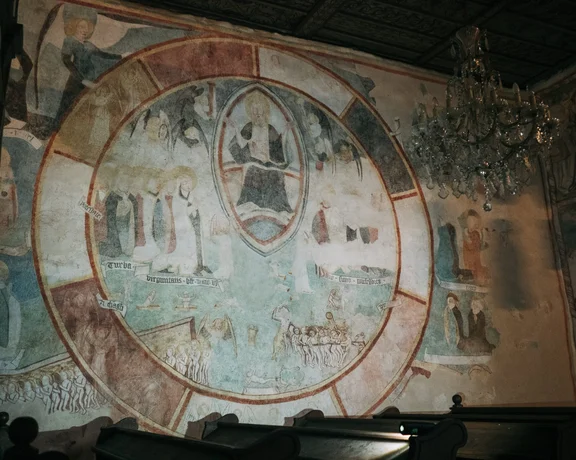 Interior of the Gothic church in Kyjatice, Slovakia, showing faded medieval wall paintings depicting a sacred scene.