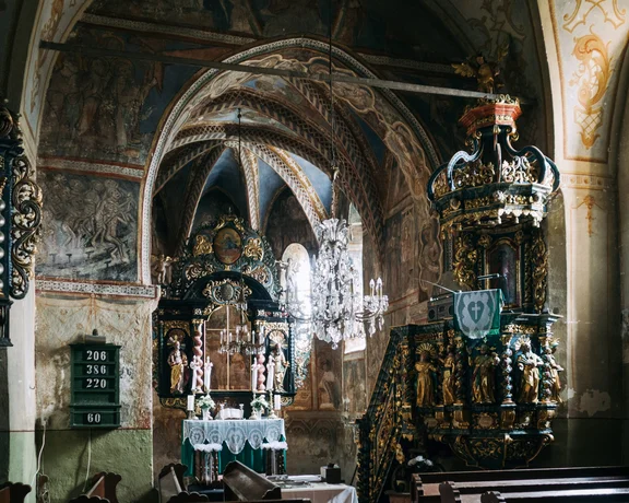 Interior of the Gothic church in Ochtiná, Slovakia, featuring medieval frescoes, stone arches, and soft natural light illuminating the historic walls.