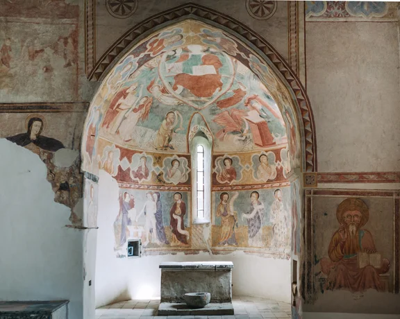 A view inside the medieval church in Rákoš, showing the colorful but faded frescoes painted on the arched wall, surrounding a narrow central window.