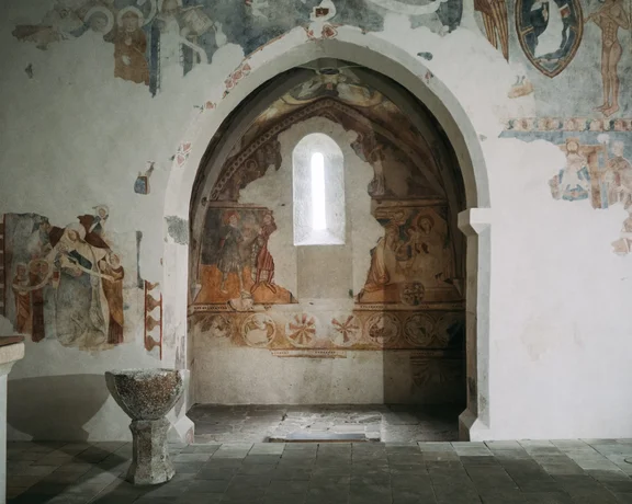 Interior of the Gothic church in Rimavské Brezovo, Slovakia, with medieval wall paintings, natural light highlighting the historic frescoes.