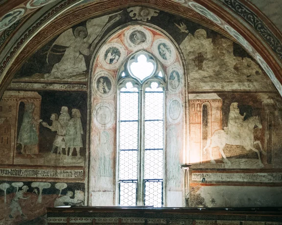 Interior of Stiknik Church in Slovakia with Gothic arched window and medieval frescoes of saints, serving as a “Bible of the poor” that reflects rural European art heritage.