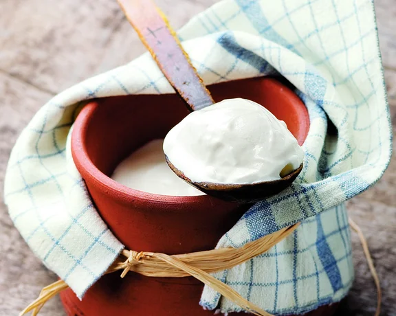 Traditional Bulgarian yogurt served in a clay pot with a wooden spoon and covered with a cloth.