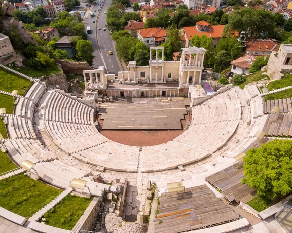 Vue aérienne du théâtre romain antique de Plovdiv, en Bulgarie, montrant les gradins en marbre en demi-cercle, la scène et le panorama urbain environnant.
