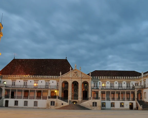 コインブラ大学のパティオ・ダス・エスコラスが夜にやわらかく照らされ、歴史的な石造りの建物と星空の下に広がる静かな中庭が映し出されている。