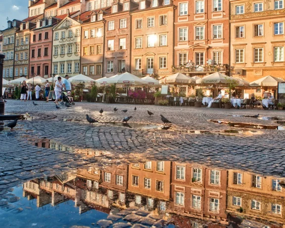 Colorful historic buildings reflected in puddles on a cobblestone square at sunset,