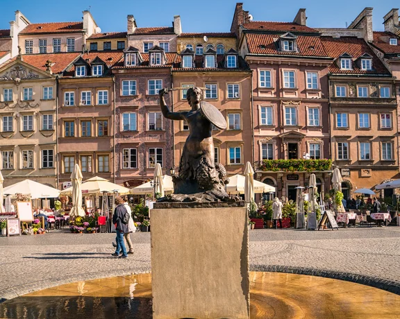 Mermaid statue fountain in a historic old town square with colorful townhouses and cafés
