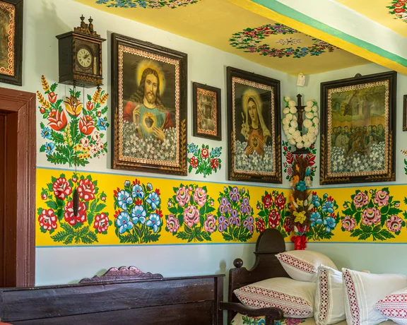 Traditional room with vibrant floral wall art, religious icons, and a neatly made bed.