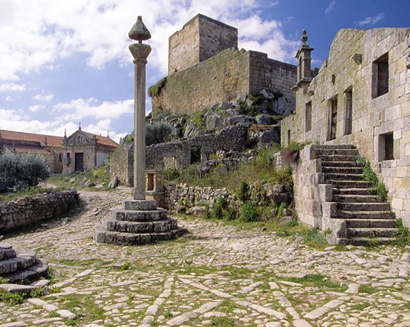 Stone ruins and cobbled streets in the historic village of Marialva, Portugal, with a medieval castle in the background.