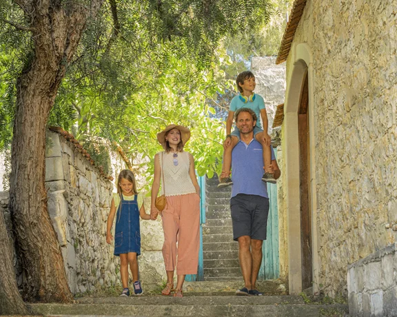 Family of four walking down a stone path in summer by an old building and trees.