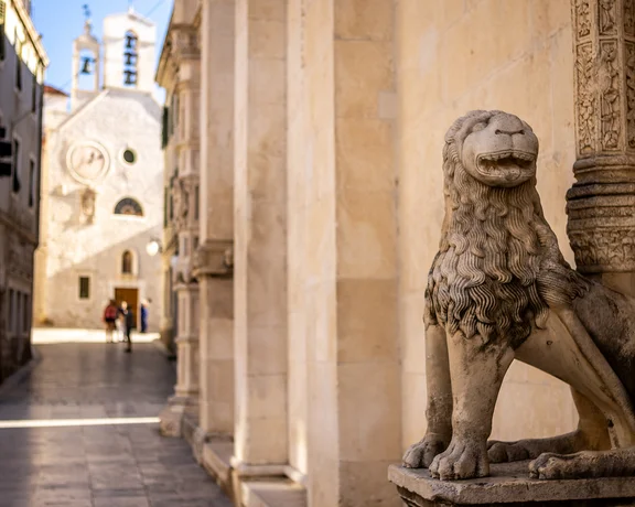 Stone lion statue on a sunlit street beside historic buildings.