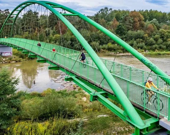 Green pedestrian bridge over a river with people walking and cycling.