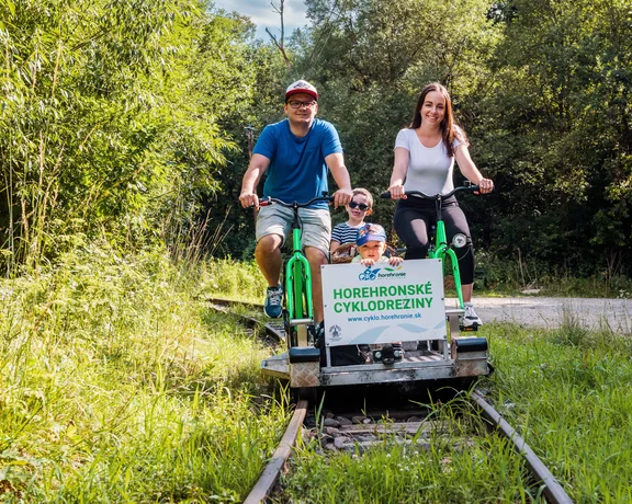 Family riding a rail bike through a lush green forest on a sunny day.