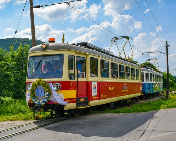 Vintage red and yellow tram decorated with flowers on a sunny day in the countryside.