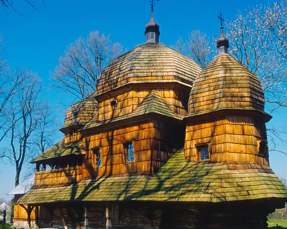 Wooden church with domed roofs, surrounded by leafless trees under a clear blue sky.