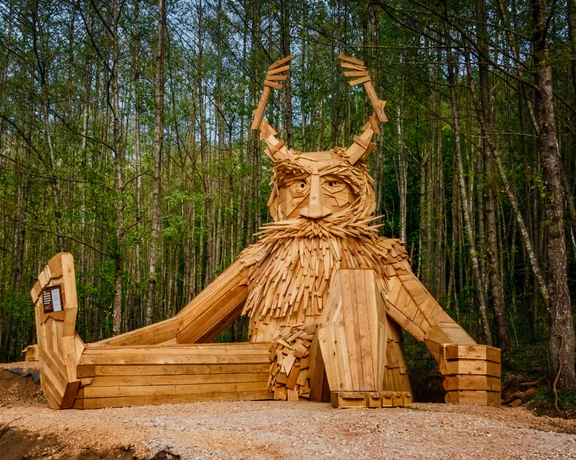 Large wooden troll sculpture sitting in a forest clearing.