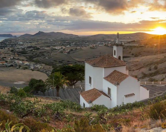 White church on a hillside overlooking a coastal town at sunset.