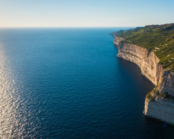 Steep cliffs meeting a calm blue sea under a clear sky at sunset.