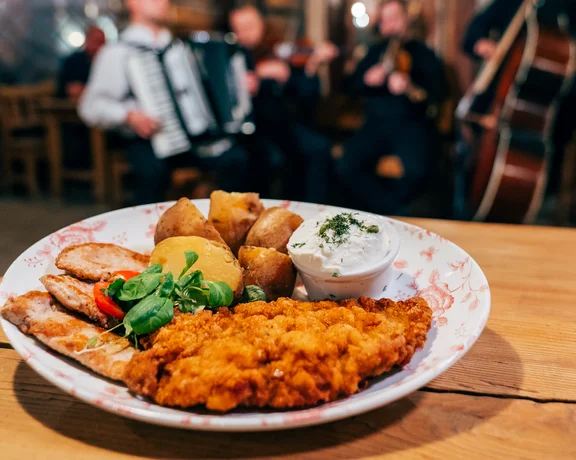 Plate of fried schnitzel, potatoes, and salad on a wooden table, band playing in background.