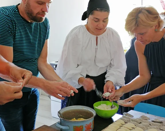 Four people preparing food together at a table, filling and folding dough.