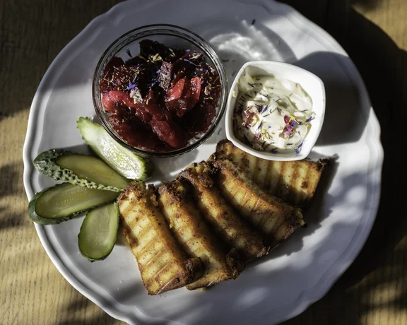 Grilled cheese rolls with pickles, beet salad, and creamy dip on a white plate.