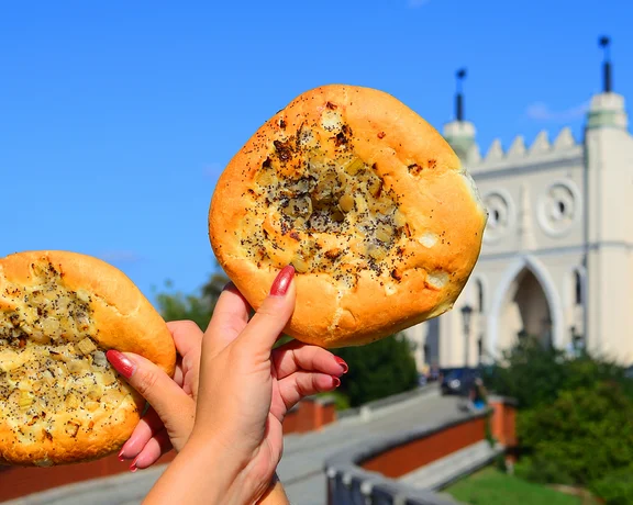 Two hands holding round bread topped with seeds, castle building in the background.