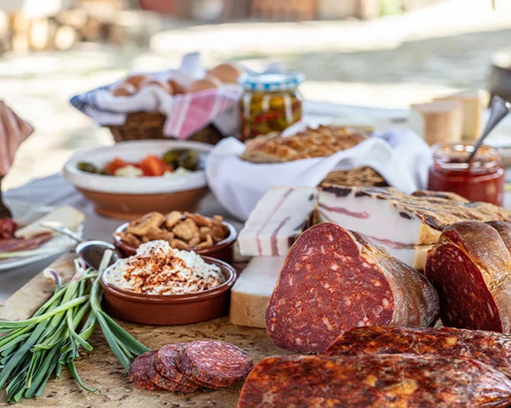 Charcuterie board with assorted meats, cheeses, bread, and fresh vegetables on an outdoor table.