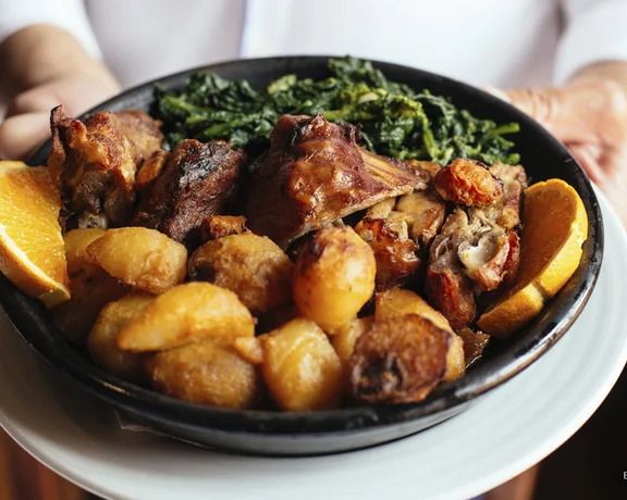 Plate of roasted meat, potatoes, greens, and orange slices held by a person in a white shirt.