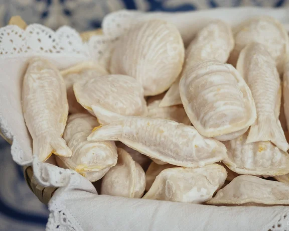 Tray of fish-shaped pastries dusted with powdered sugar on a lace-lined basket.