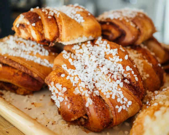 Fresh cinnamon rolls topped with pearl sugar on a wooden tray.