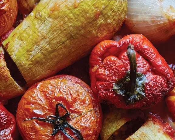 Roasted stuffed peppers, tomatoes, and zucchini in a baking dish.