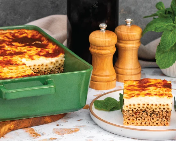 Baked pasta dish with golden top in green pan, slice served on plate with fork and mint garnish.