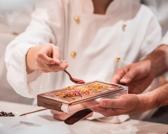 Chef garnishing a chocolate dessert bar with toppings.