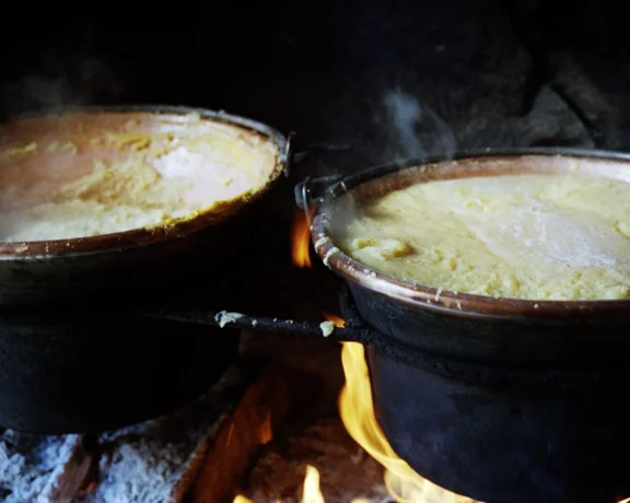Two large pots of polenta cooking over an open fire.