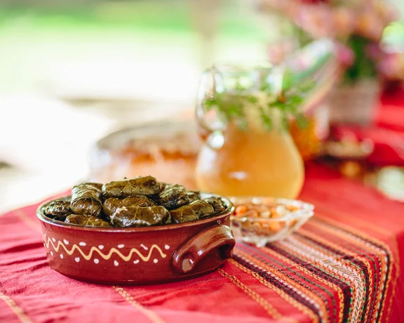 Ceramic dish of stuffed grape leaves on a red embroidered tablecloth.