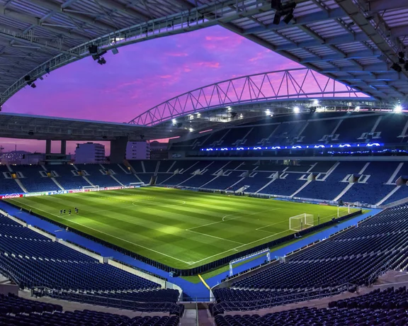 Empty soccer stadium under a purple sunset sky, green field illuminated.