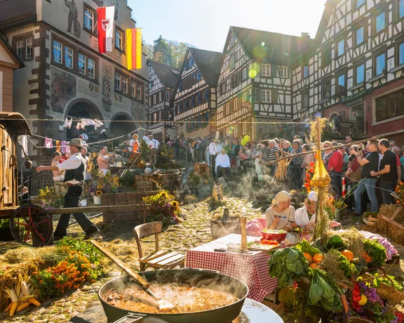Outdoor festival in a cobblestone square with people, flowers, and food stands.