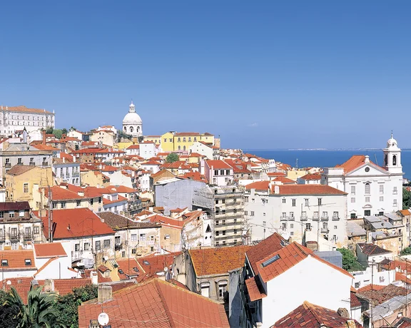 Red-roofed buildings on a hillside overlooking the sea under a clear blue sky.