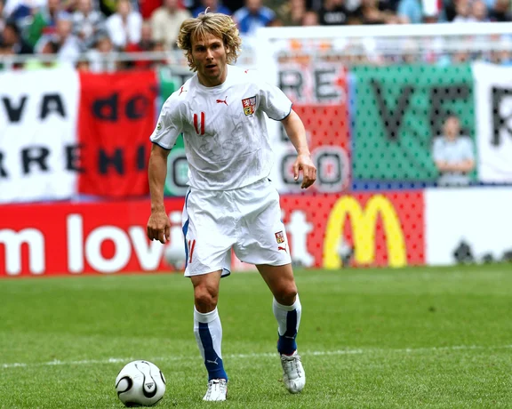Soccer player in white jersey dribbling ball on green field during a match.