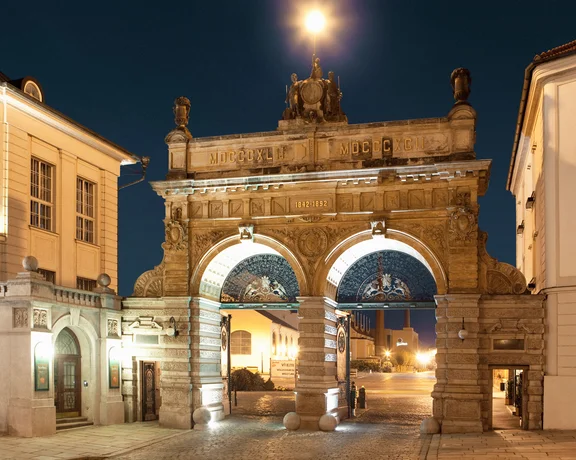 Stone archway illuminated at night between two historic buildings.