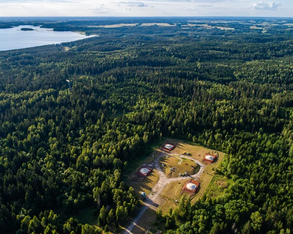 Aerial view of a forest clearing with several small buildings and a lake in the distance.