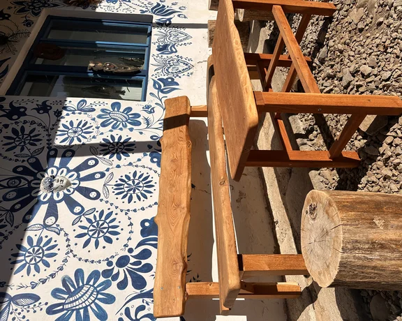 Wooden table and benches beside a wall with blue floral patterns and a window.