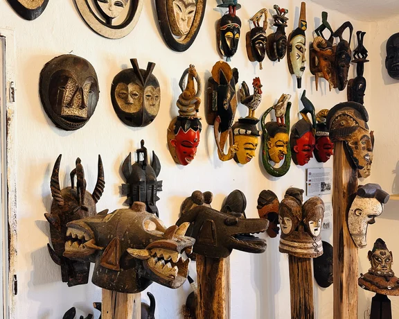Wall displays of colorful, carved wooden masks and mask sculptures on stands in a gallery.