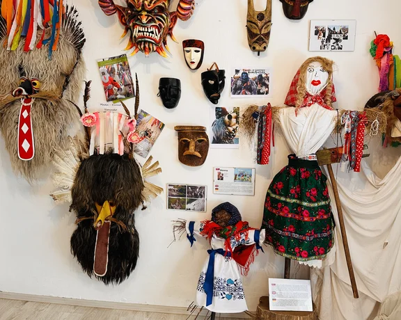 Colorful traditional masks and costumes displayed on a white wall and mannequins.